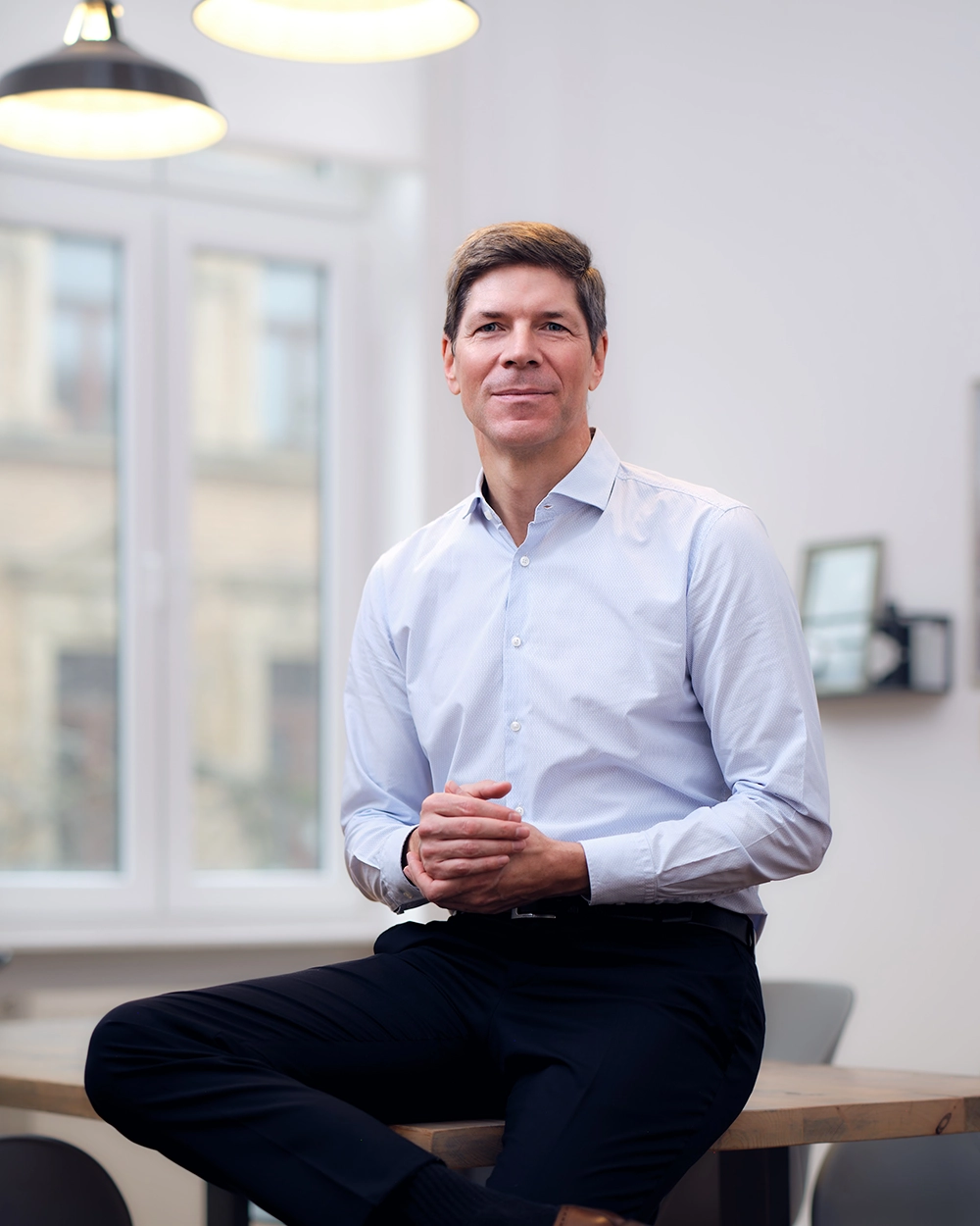 Prof. Dr. Alexander Hofmann sitzend an der Kante eines großen Tisches in einem Besprechungsraum.